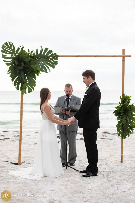 bride-groom-officiant-in-front-of-bamoo-arch-with-tropical-grns