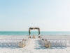 Beach Ceremony Site with Cedar Arch Draped with Fabric, Pink and Peach Flowers and Lanterns with Flowers at Back of Aisle